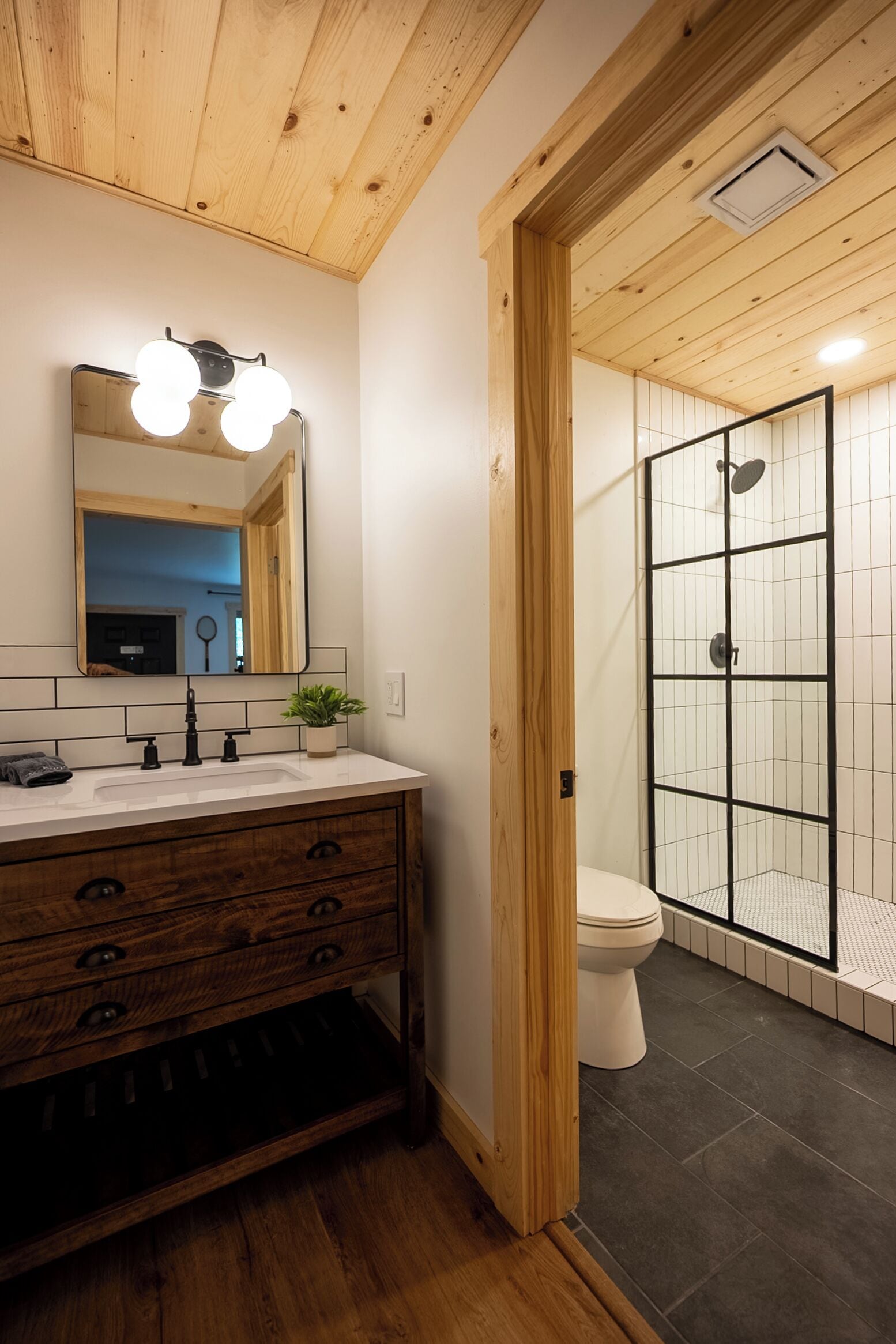 Une salle de bain avec un meuble-lavabo en bois, un miroir avec éclairage intégré, une plante et un espace douche.