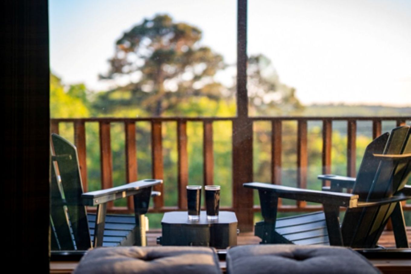 Une terrasse avec deux fauteuils Adirondack et une petite table, donnant sur une zone boisée.