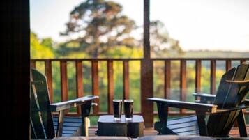 Une terrasse avec deux fauteuils Adirondack et une petite table, donnant sur une zone boisée.