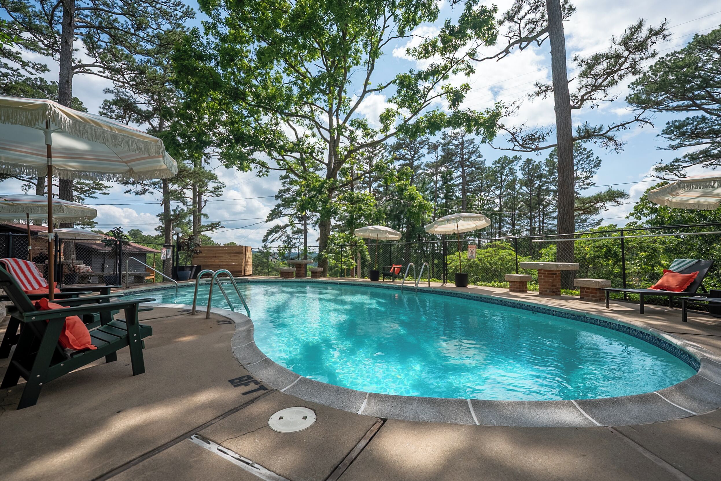 A swimming pool with lounge chairs and umbrellas, surrounded by trees.