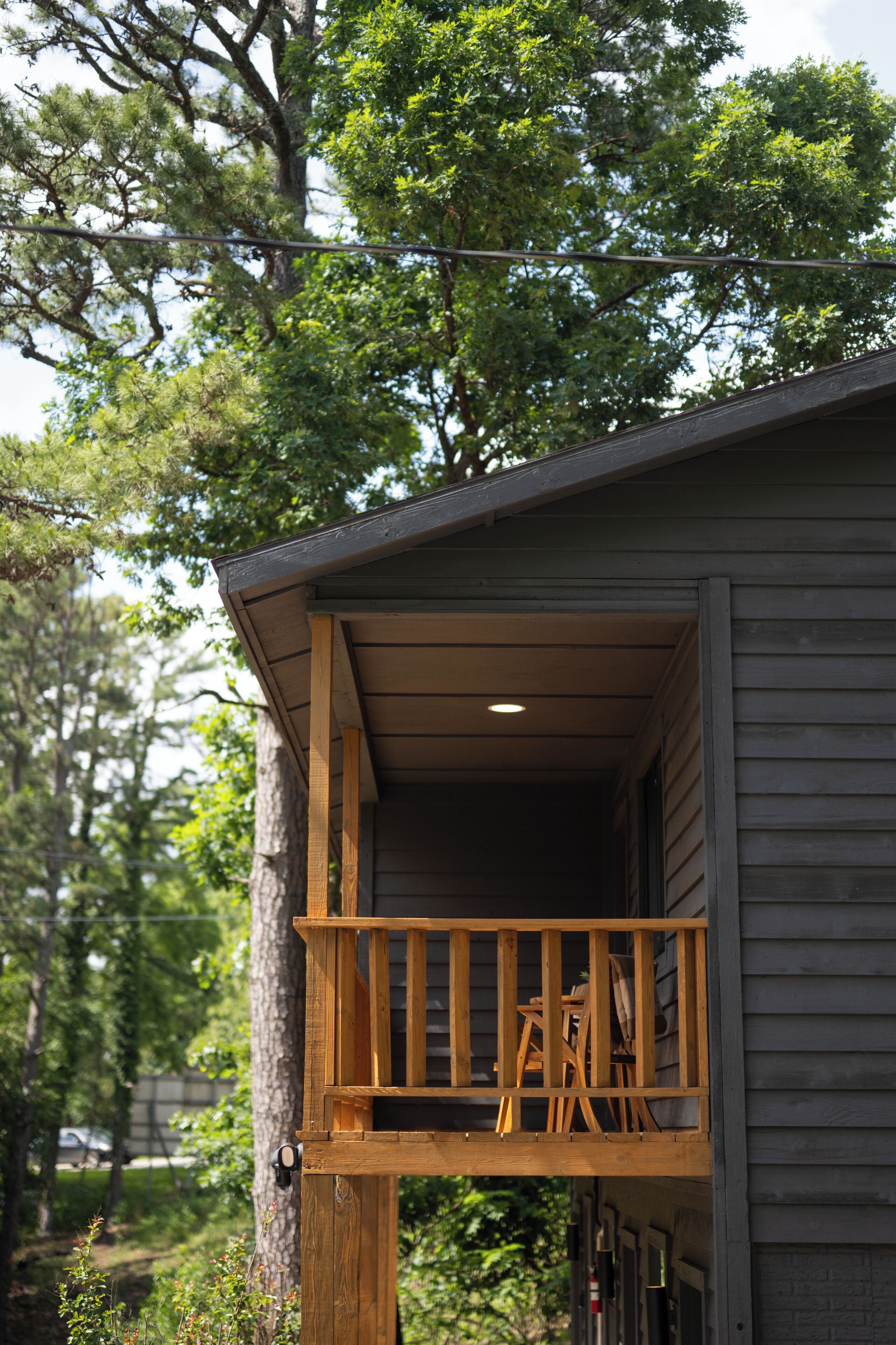 A wooden balcony with a railing, a ladder, and a door leading to a covered porch area.