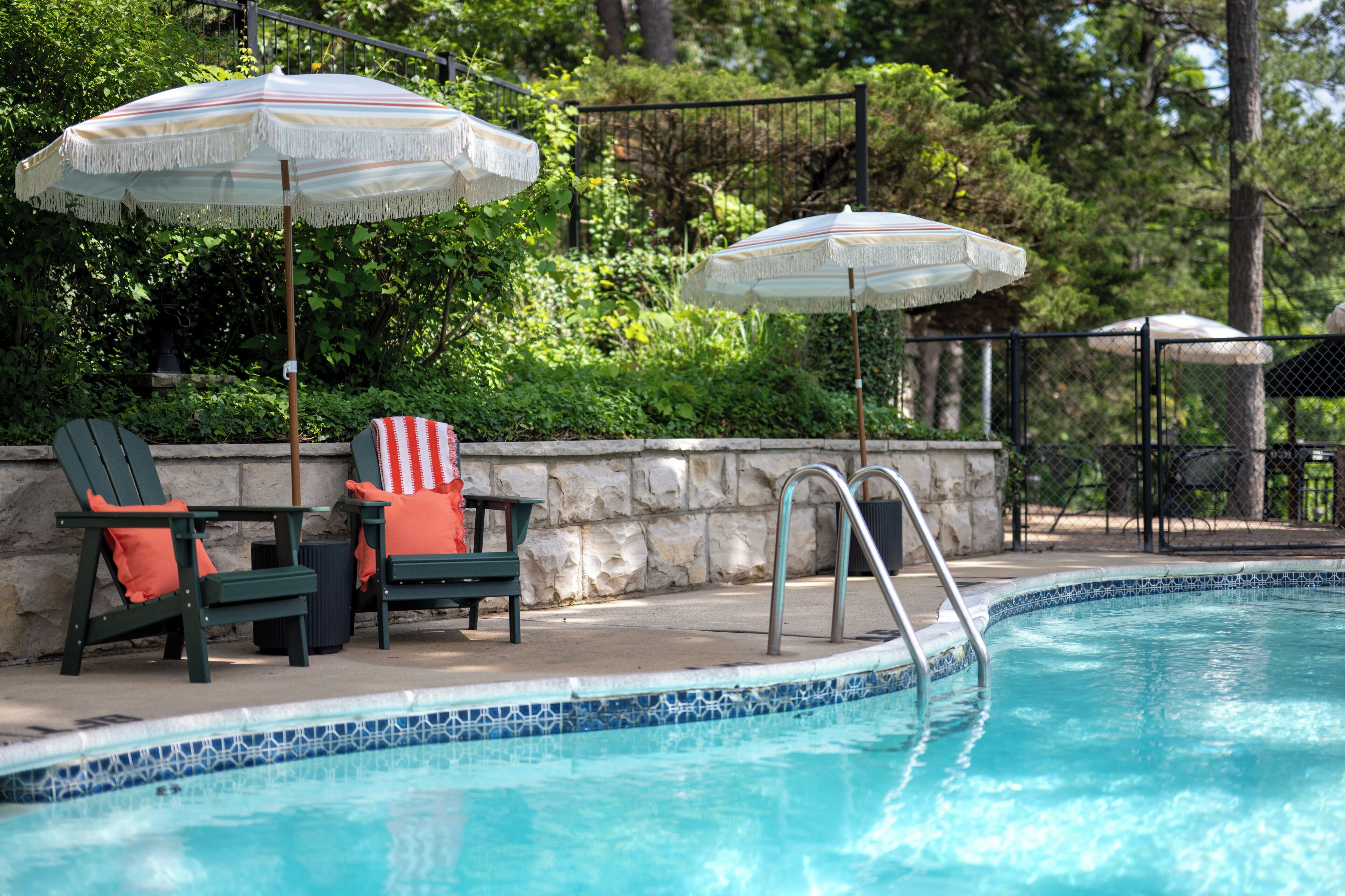 A pool area with two chairs, an American flag, and two umbrellas.
