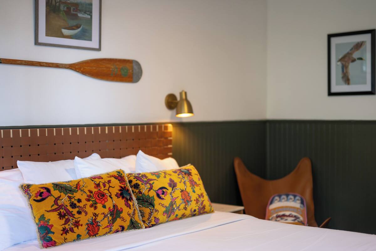 A hotel room with a bed, a wooden paddle on the wall, a lamp, and a chair.