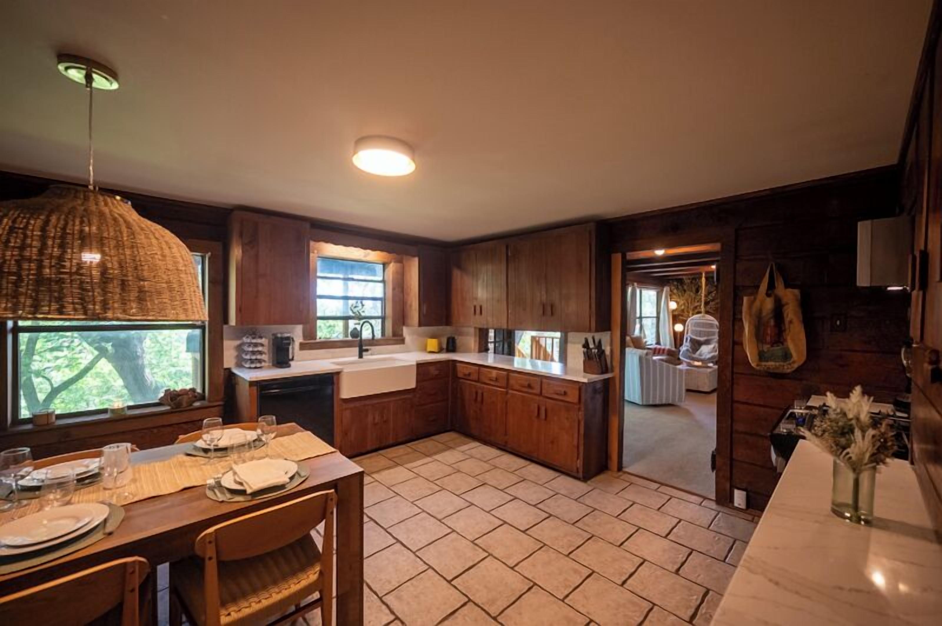 Una cocina con armarios de madera, una mesa de comedor para cuatro personas y un ventanal que proporciona luz natural.