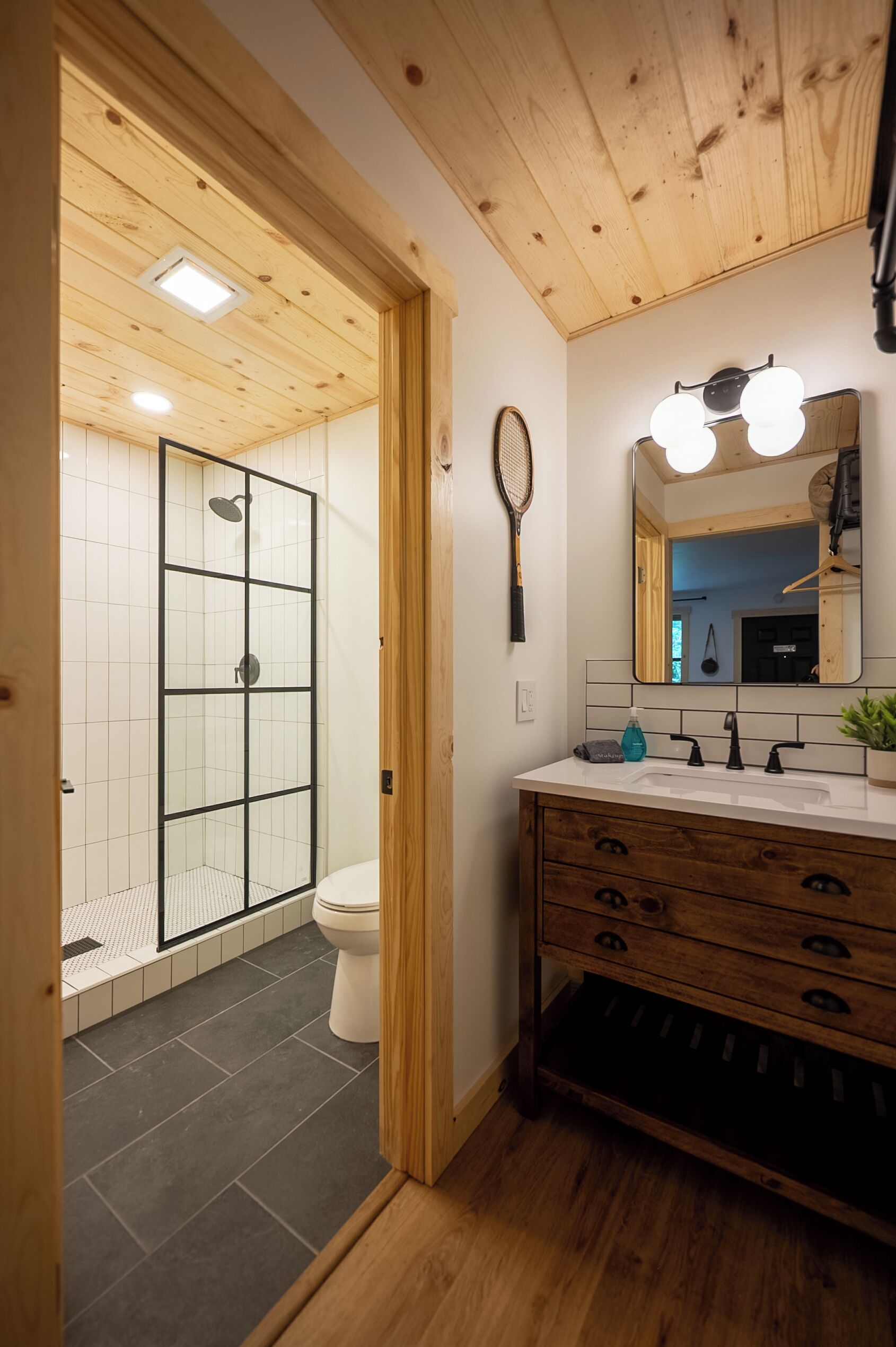 A bathroom with a wooden ceiling, a glass shower enclosure, a white toilet, and a vanity with a mirror and lights.