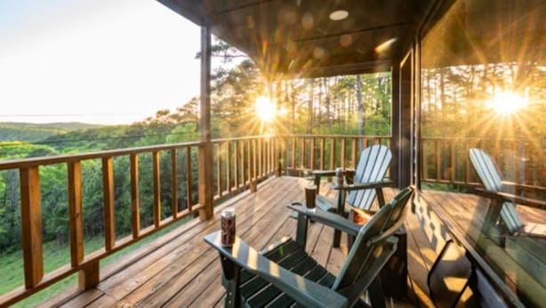 Een houten terras met stoelen en een tafel, met uitzicht op een bebost landschap.