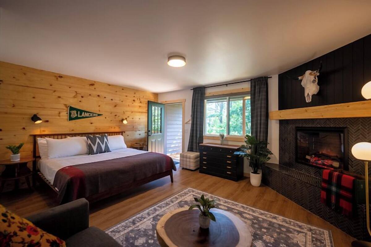 A cozy log cabin-style bedroom with a large bed, a fireplace, and a view of the outdoors.