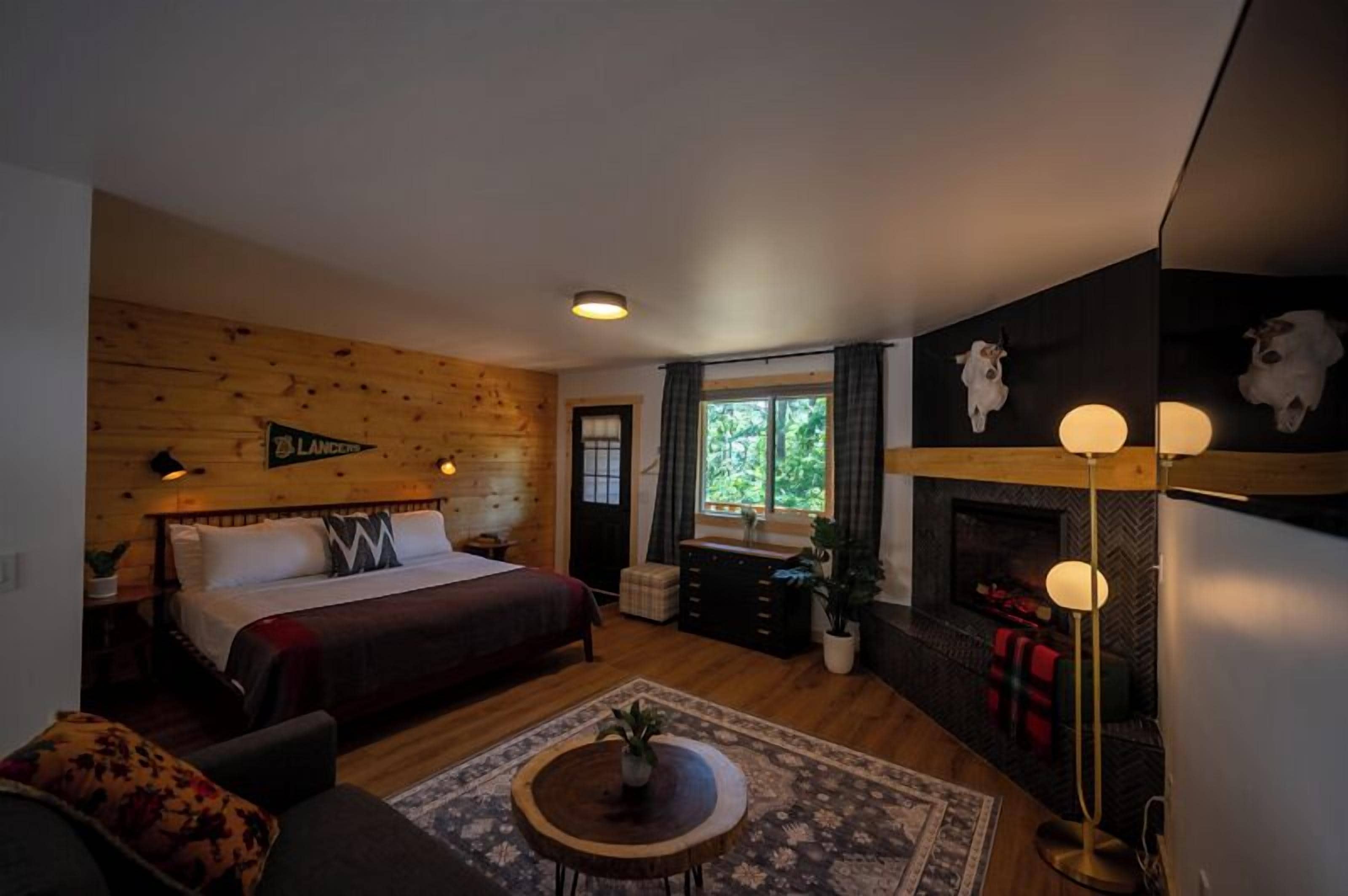 Una habitación acogedora con cama, sofá, chimenea y pared de madera.