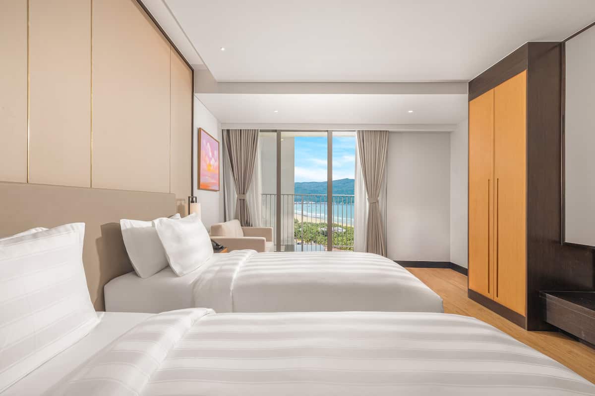 Habitación de hotel con una cama grande, un sofá, un televisor y un balcón con vistas al mar.