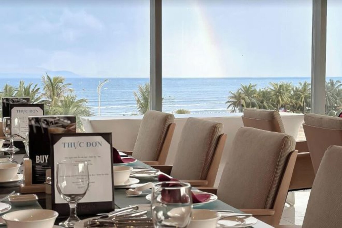 A dining table set for two with a view of the ocean, a sign indicating a Thuc Doan purchase, and a menu.