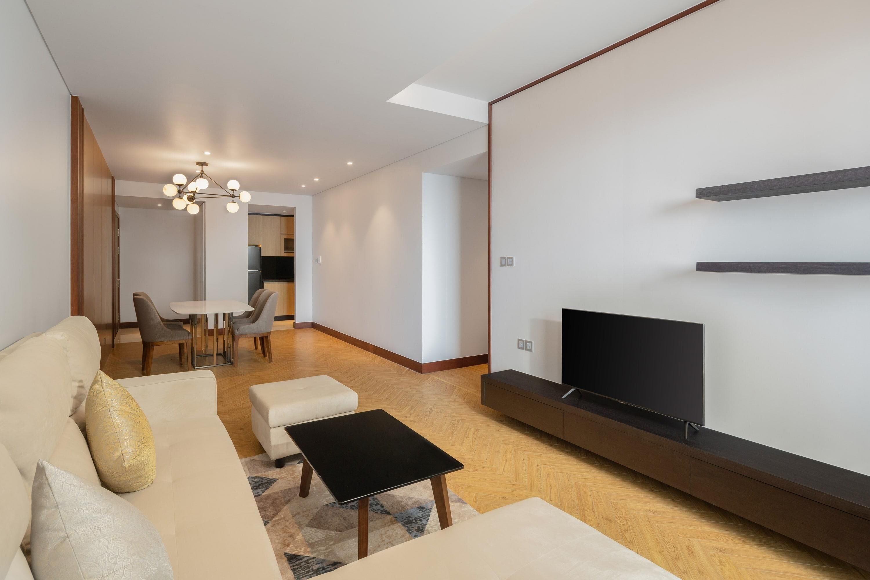 Una sala moderna con sofá, reposapiés, mesa de centro negra, televisor y un comedor con sillas y mesa.