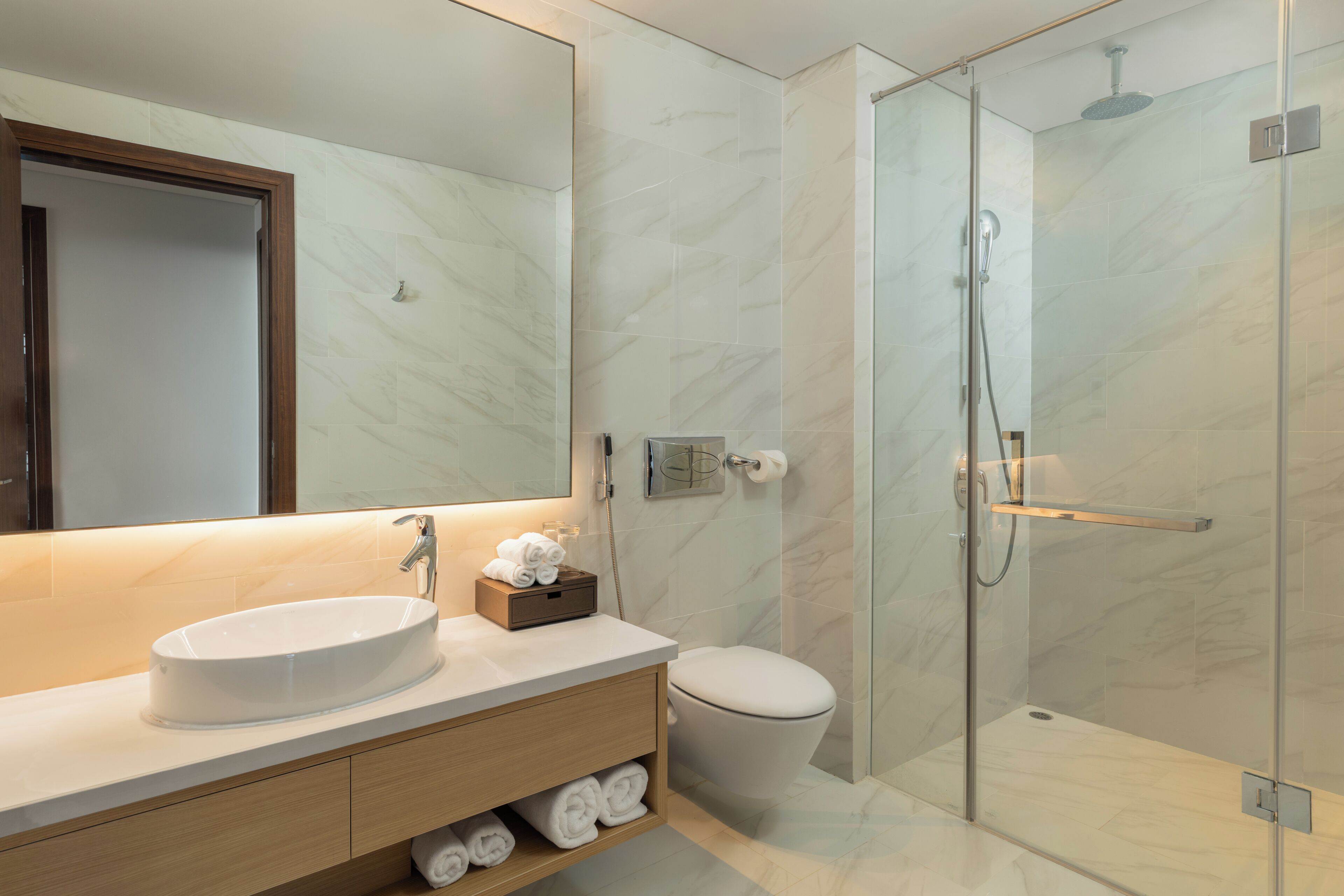 A modern bathroom with a large mirror, a white sink, a toilet, and a glass-enclosed shower area.