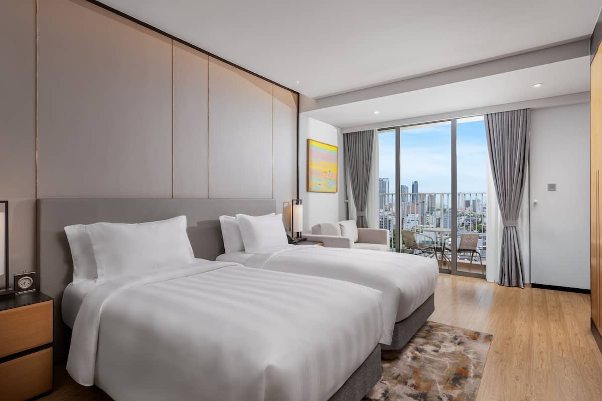 Habitación de hotel moderna con dos camas grandes, vistas a la ciudad, un balcón y un amplio ventanal con cortinas.