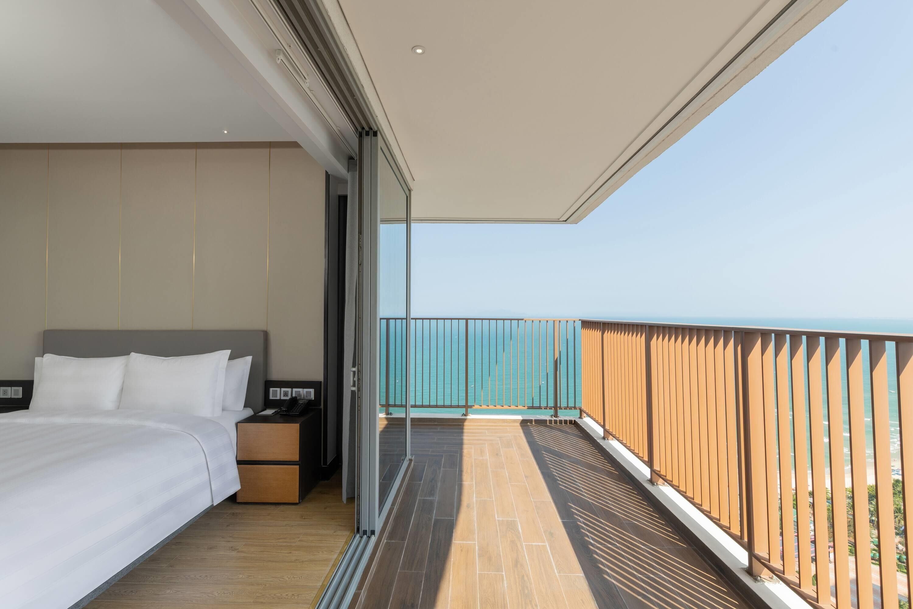 A bedroom with a large bed, a nightstand, and a view of the ocean through a balcony.