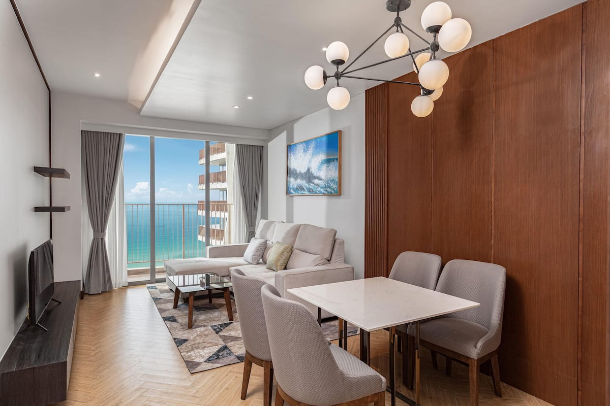 Una sala de estar moderna con sofá, mesa de comedor, sillas, televisor y vista al océano.