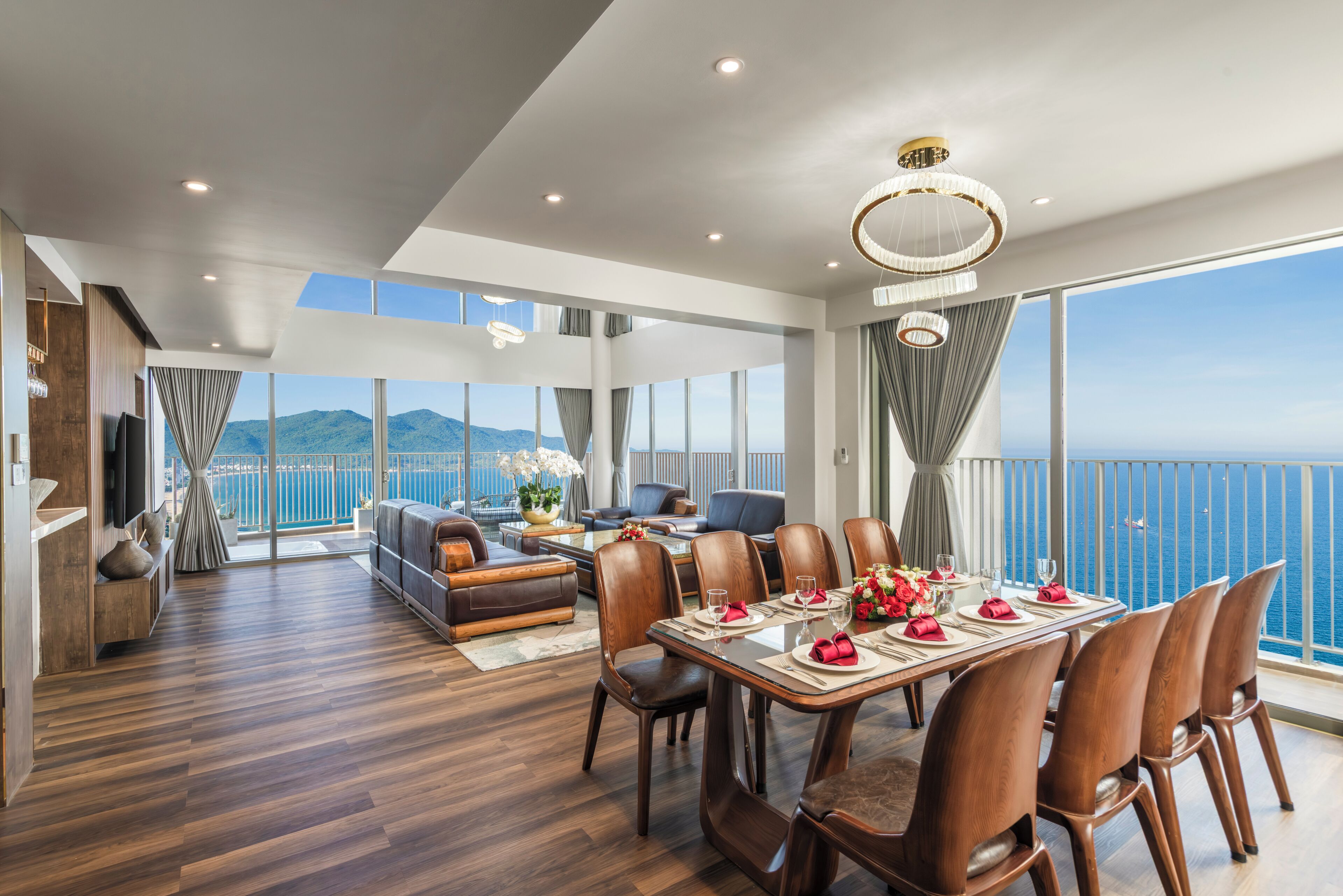 Ein moderner Essbereich mit Meerblick, Holzböden und einer Chandelüster.