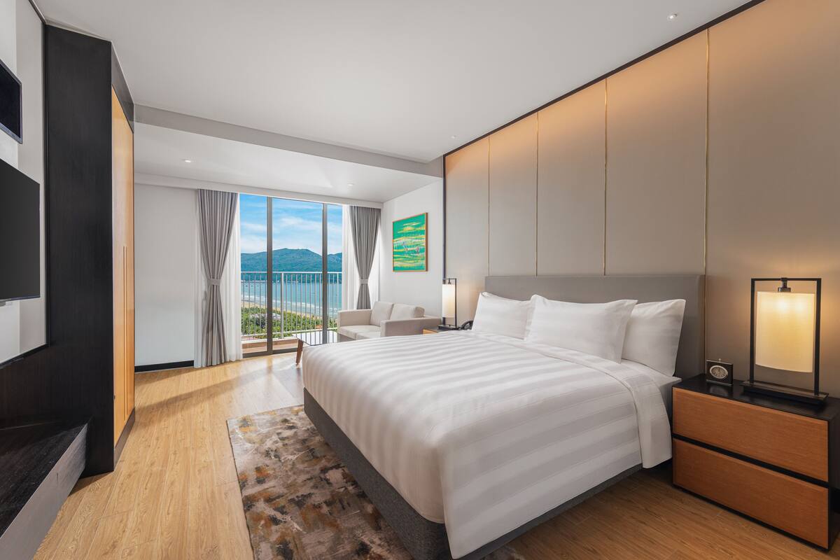 Una habitación de hotel moderna con una cama grande, televisión, escritorio y balcón con vistas.