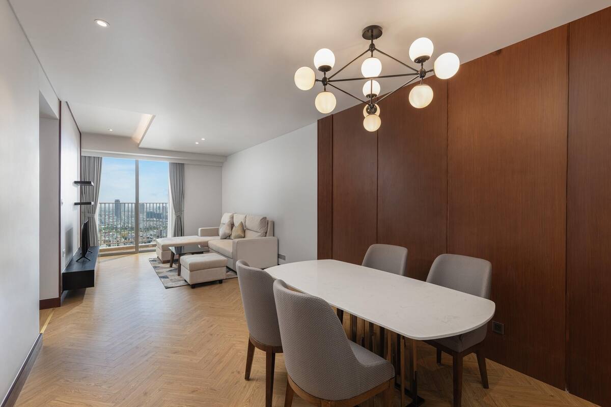 Un comedor moderno con una mesa y sillas blancas, un revestimiento de pared de madera y vistas a la ciudad a través de grandes ventanales.