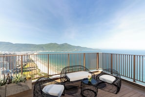Un balcon agrémenté de meubles en osier, d’une petite table et offrant une vue sur l’océan et le paysage urbain.