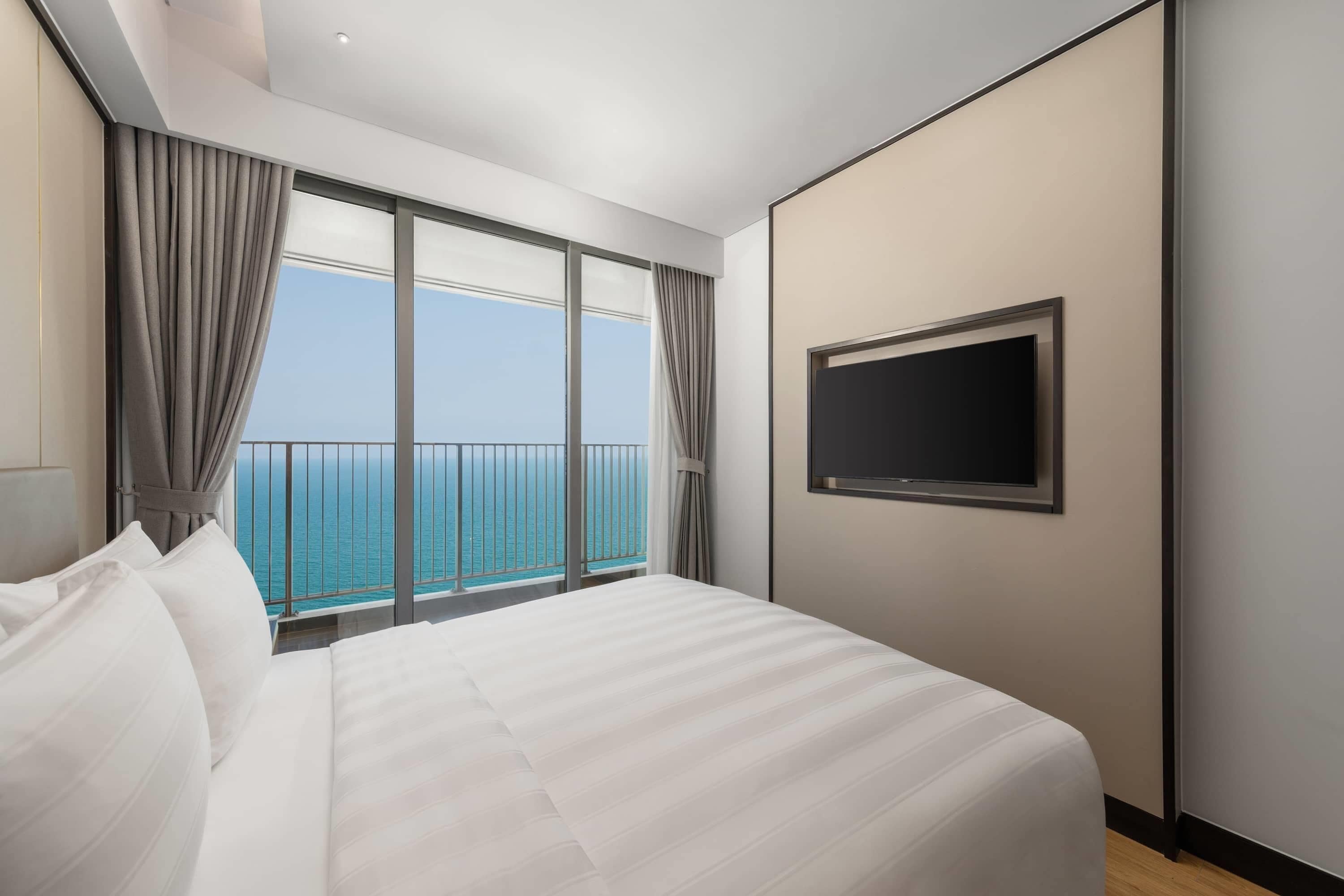 Ett hotellrum med en stor säng, en tv som är monterad på väggen och en balkong med utsikt över havet.