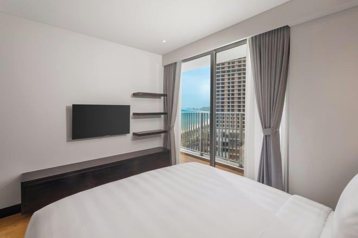 A modern hotel room with a large bed, a flat-screen TV mounted on the wall, and a balcony with a city view.