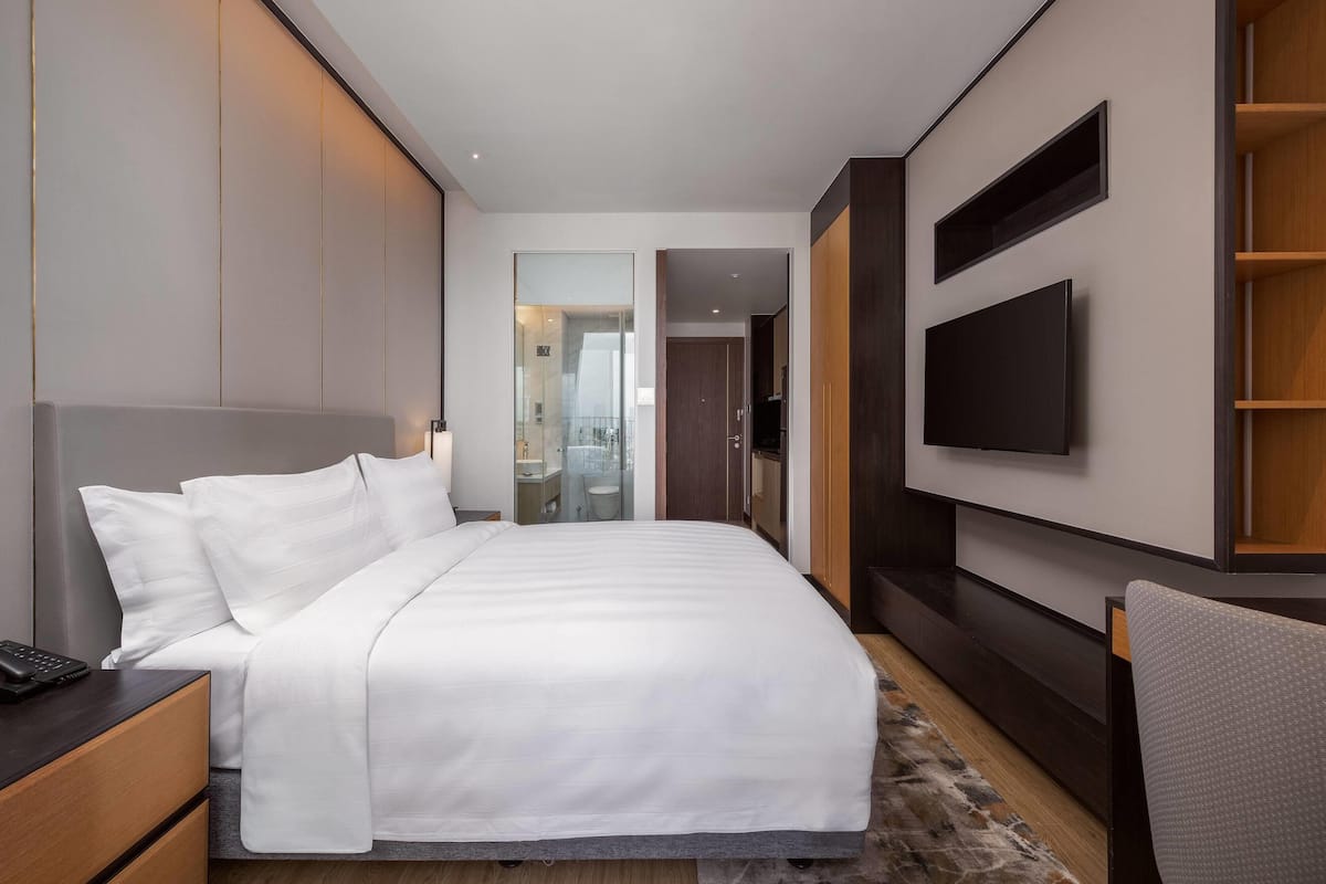 Una habitación de hotel moderna con una cama grande, un televisor de pantalla plana en la pared, una mesita de noche de madera y un escritorio con una silla.