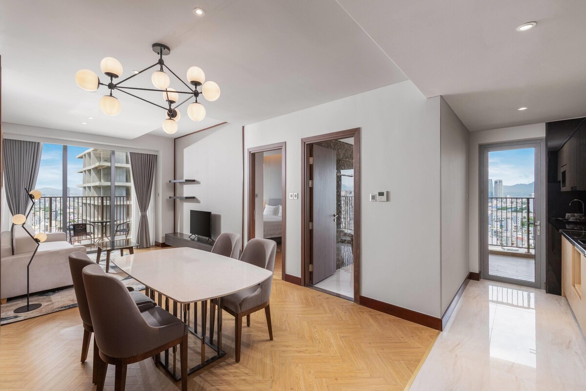A modern living room with a dining area, a sofa, a TV, and a balcony with a city view.