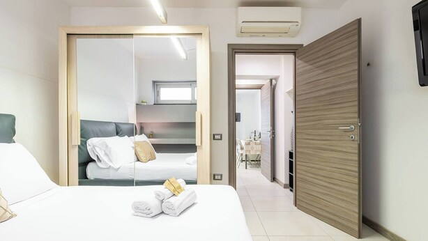 Une chambre d’hôtel avec un lit, une armoire et une salle de bain visible à travers la porte d’un placard à miroir.