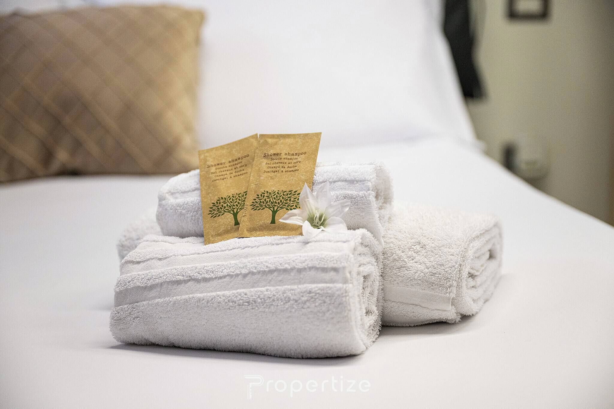 Un lit bien fait, avec des serviettes blanches et une petite carte indiquant le type de shampoing disponible pour la douche.