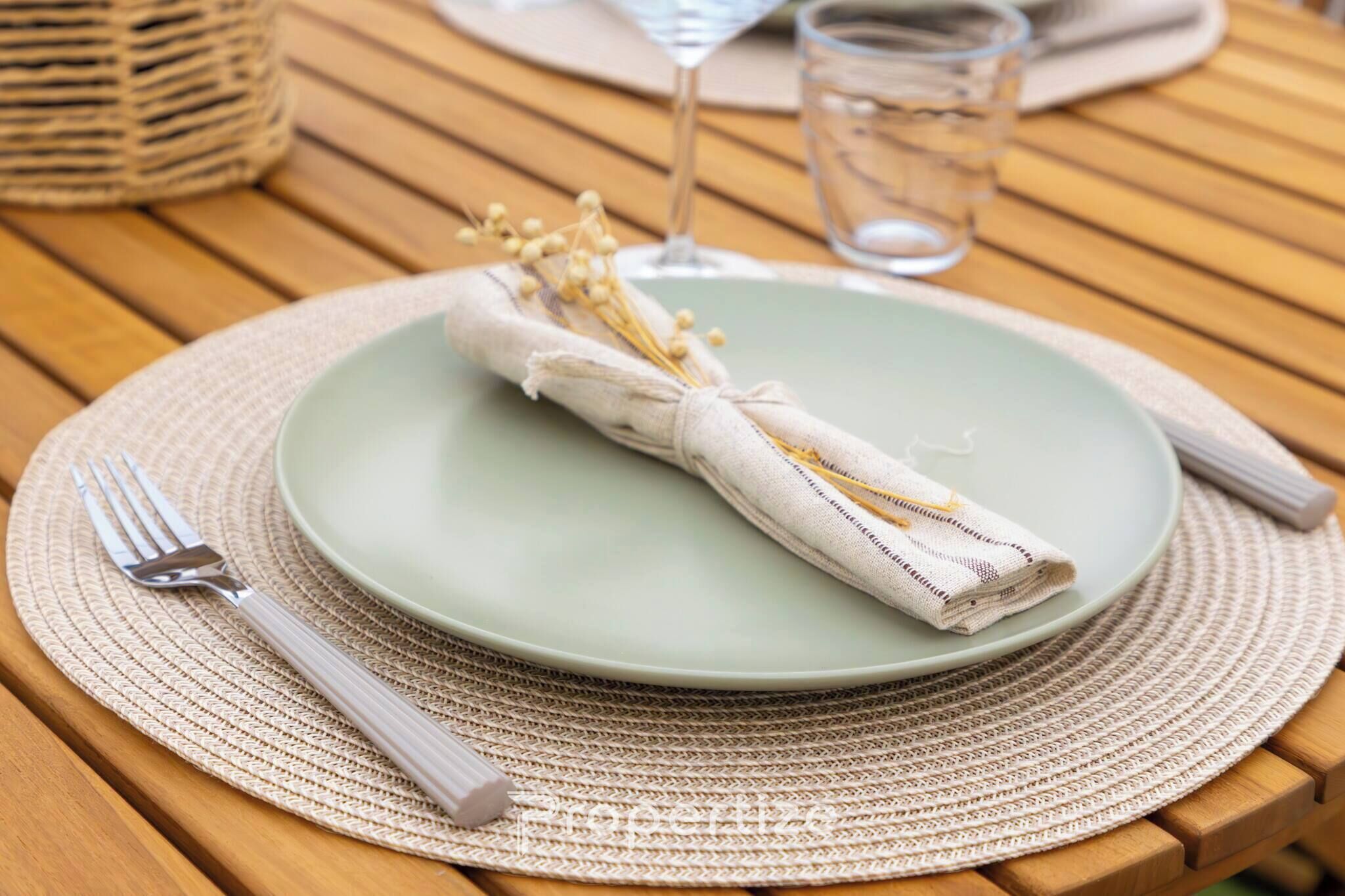 Una mesa dispuesta con un plato verde, una servilleta doblada, un tenedor, un cuchillo, un vaso de agua y una copa de vino.