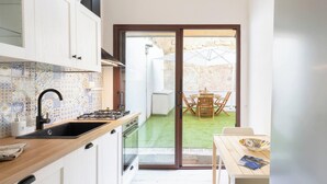 A compact kitchen with a sink, stove, and patterned backsplash. A sliding glass door leads to a patio with a table and chairs. - Alchimìa by Propertize (Cagliari)