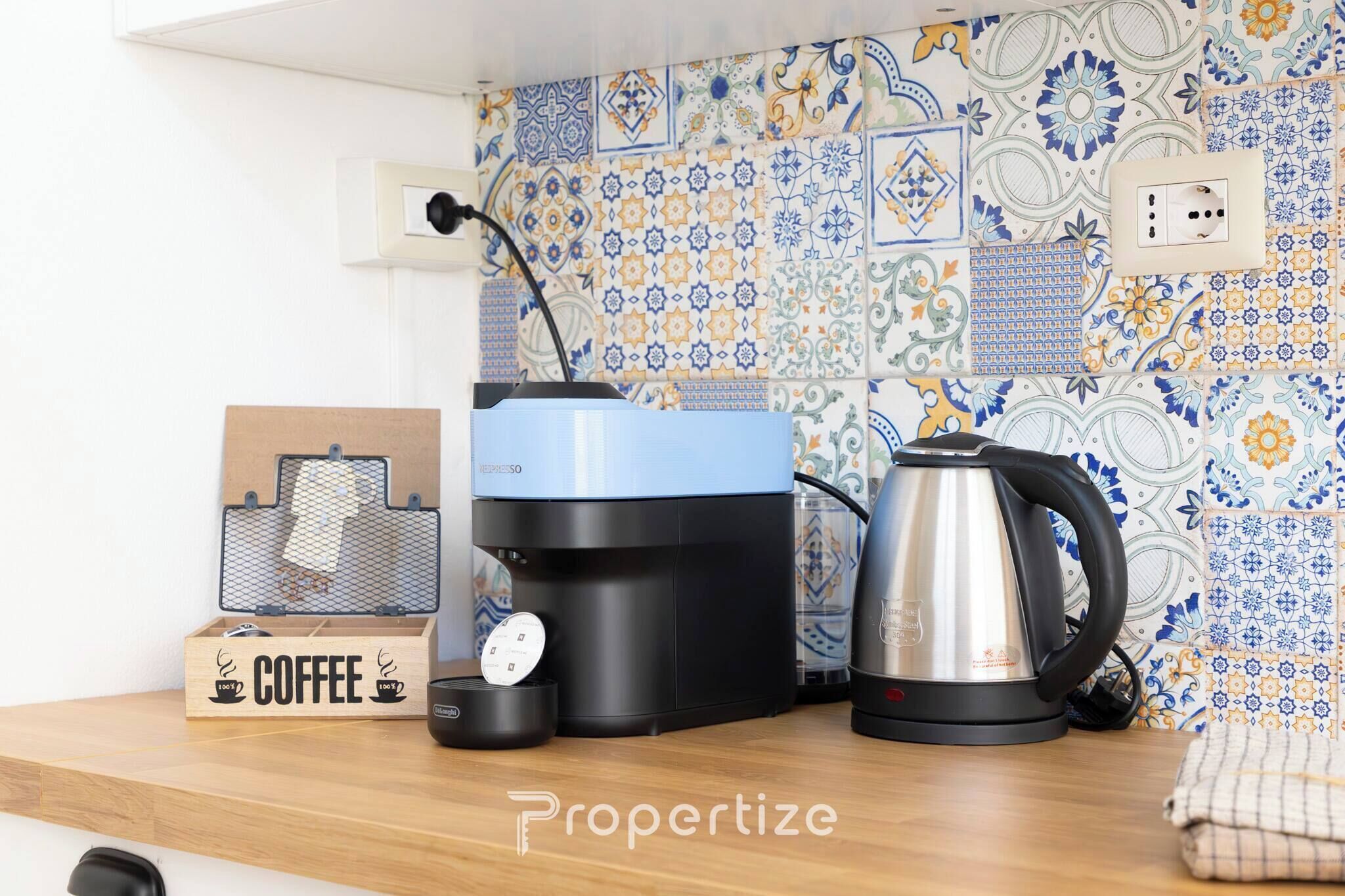 A kitchen with a coffee maker, a kettle, and a coffee-themed box on the counter.