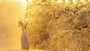 A room with a textured stone wall and a vase with flowers. - Alchimìa by Propertize (Cagliari)