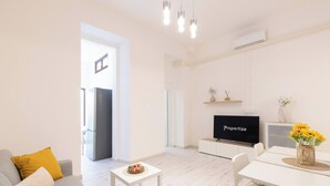 A modern living room with a flat-screen TV, a dining area, and a kitchen visible through an open door. - Alchimìa by Propertize (Cagliari)