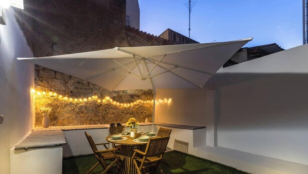 A patio with a table and chairs, a white umbrella, string lights, and a stone wall. - Alchimìa by Propertize (Cagliari)