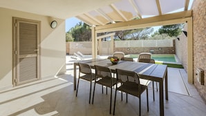 An outdoor patio with a table and chairs, a pool, and a covered area with a view of trees. - Villa Rachele ground floor apt, private pool (Porto Pinetto)