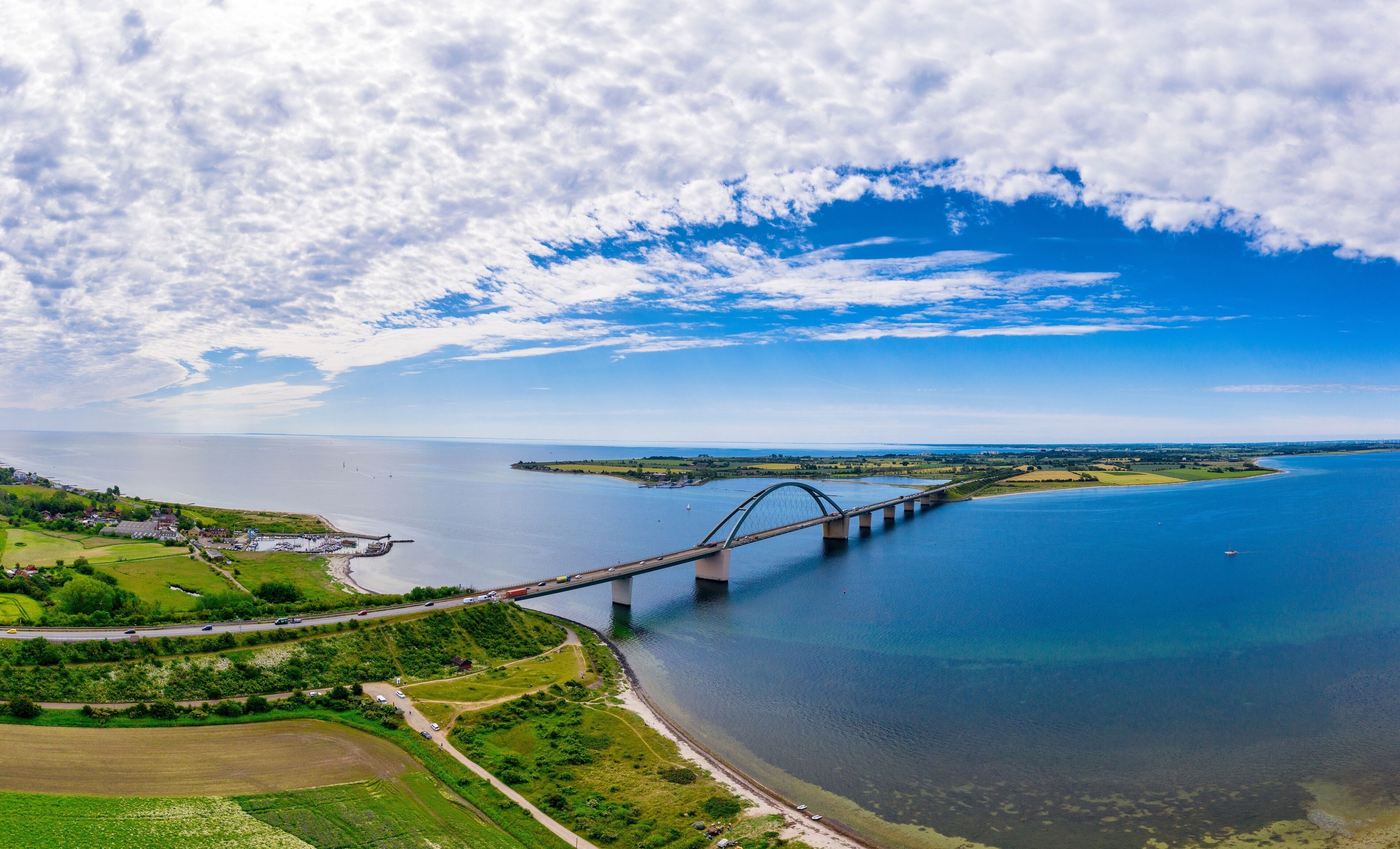 Eine große Hängebrücke über einem ruhigen Fluss, umgeben von grünen Feldern und einer kleinen Stadt.