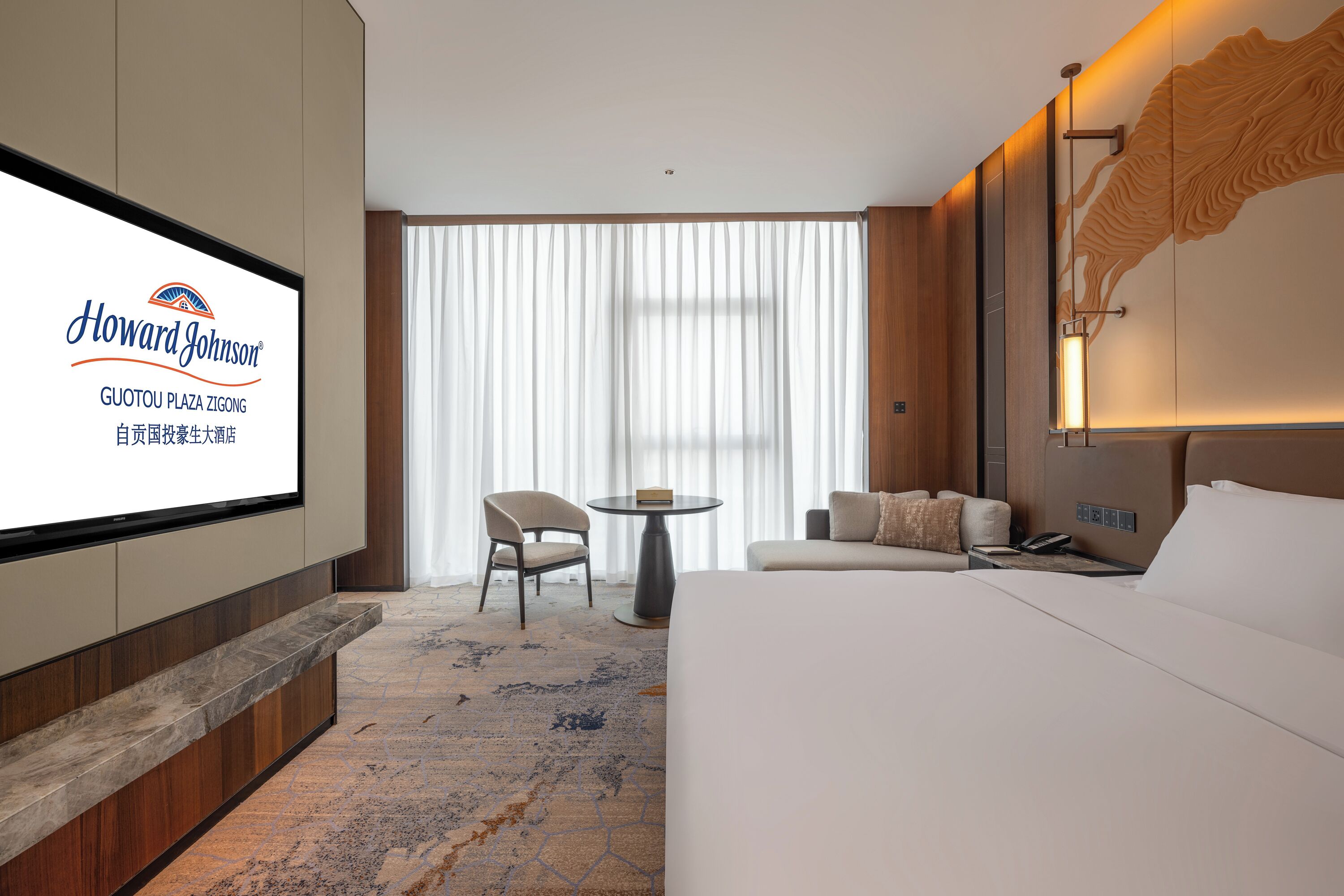 Une chambre d’hôtel avec un grand lit, un téléviseur fixé au mur, une petite table et une chaise.