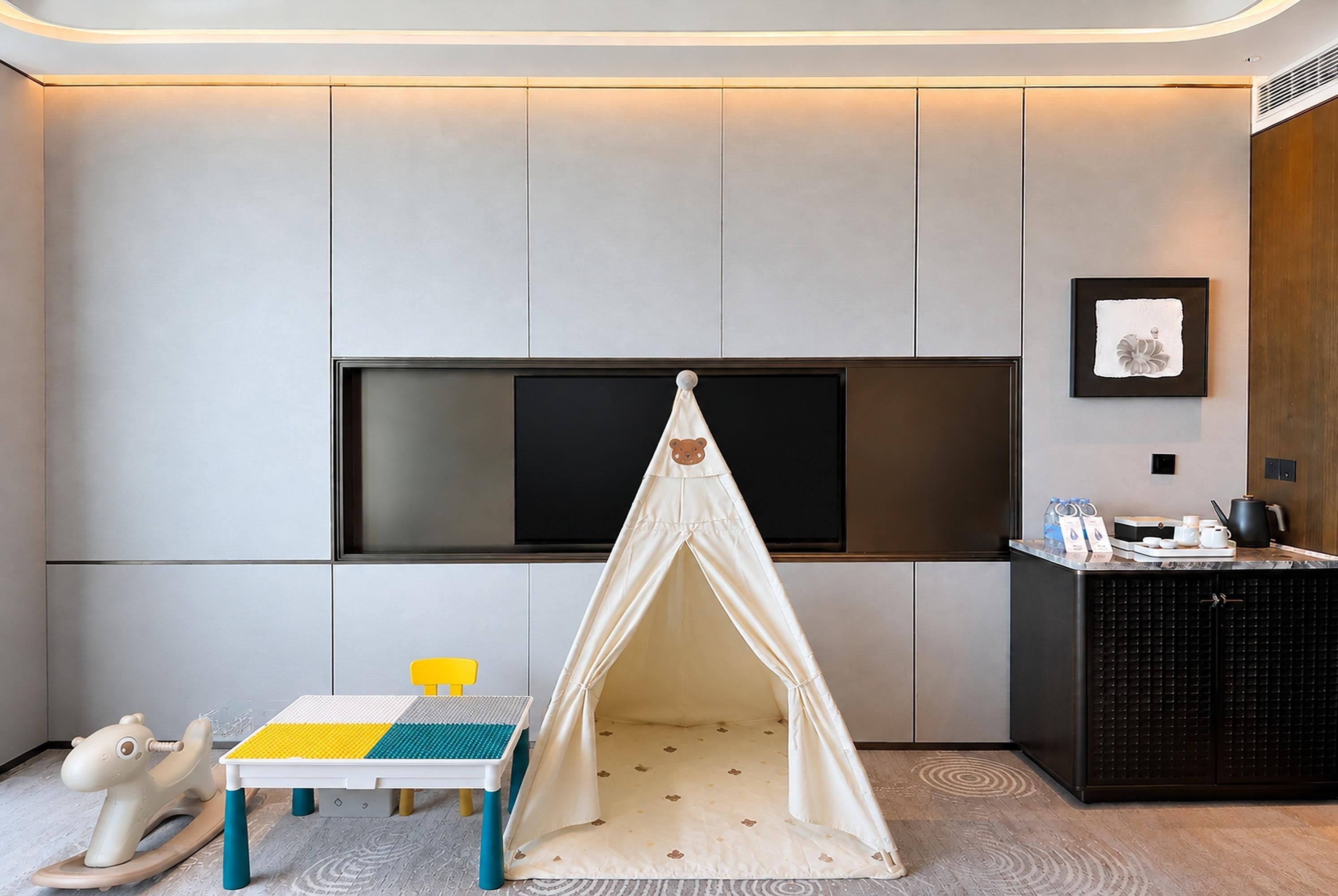 A modern room with a play tent, a small table with a colorful play mat, and a television mounted on the wall.