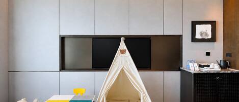 A modern room with a play tent, a small table with a colorful play mat, and a television mounted on the wall.