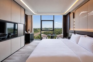 A modern hotel room with a large bed, a desk, and a TV. There is a view of a cityscape through a large window. - Howard Johnson By Wyndham Guotou Plaza Zigong (Zigong)