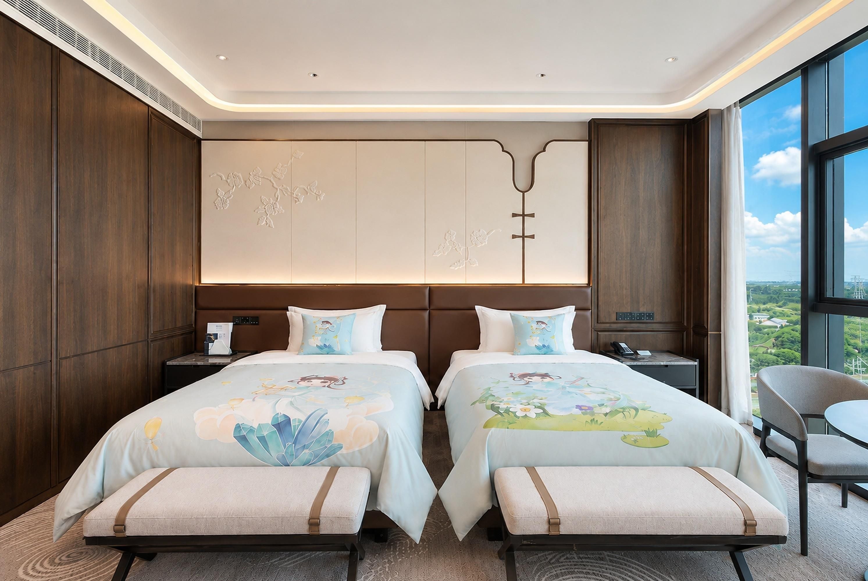 Habitación de hotel con dos camas, un ventanal amplio con vista a la ciudad, un diseño moderno en el techo y una pequeña mesa con una silla.