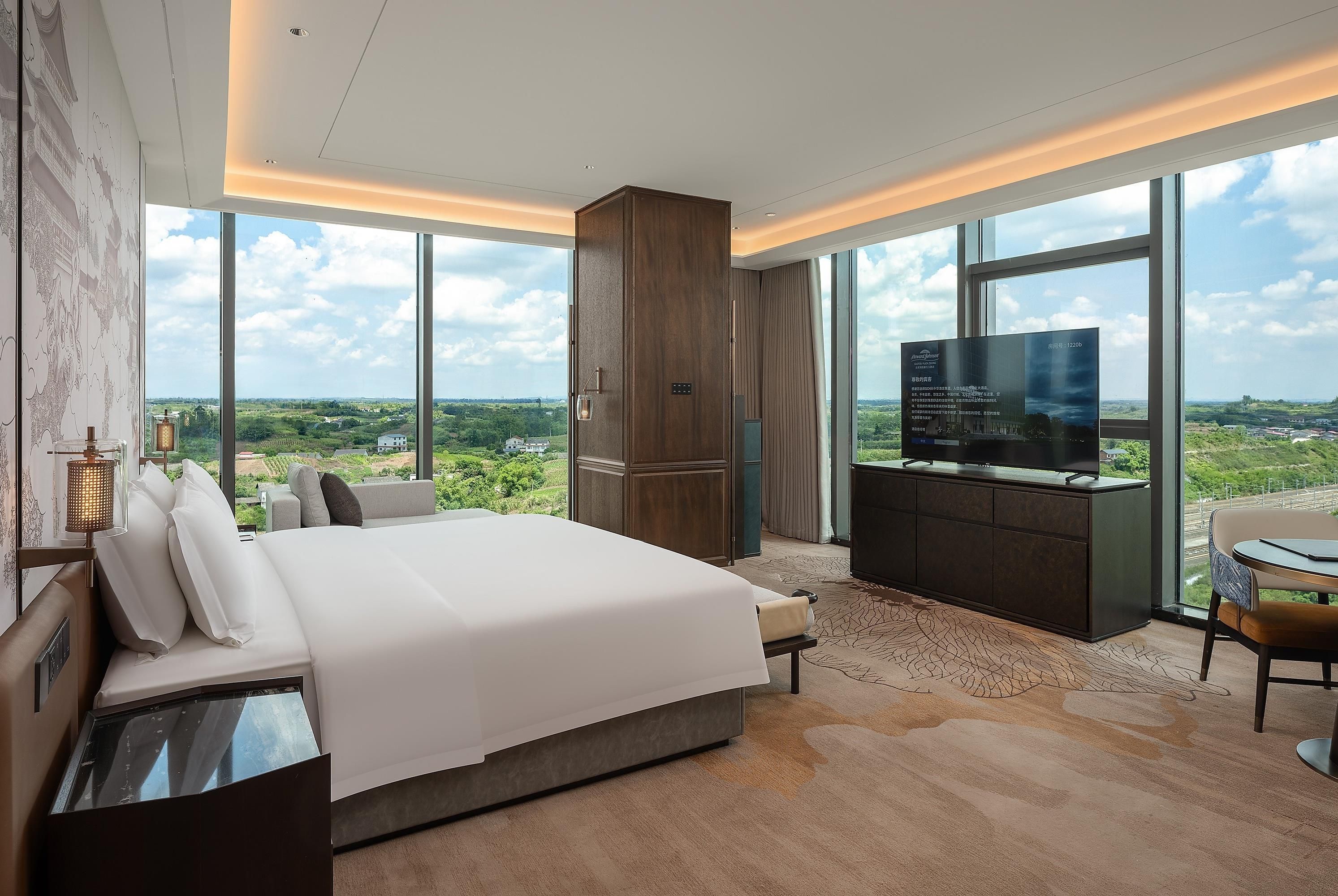 A modern hotel room with a large bed, a TV, and a view of the countryside.