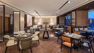 A modern dining area with round tables, comfortable seating, and a large window offering a view of the cityscape.