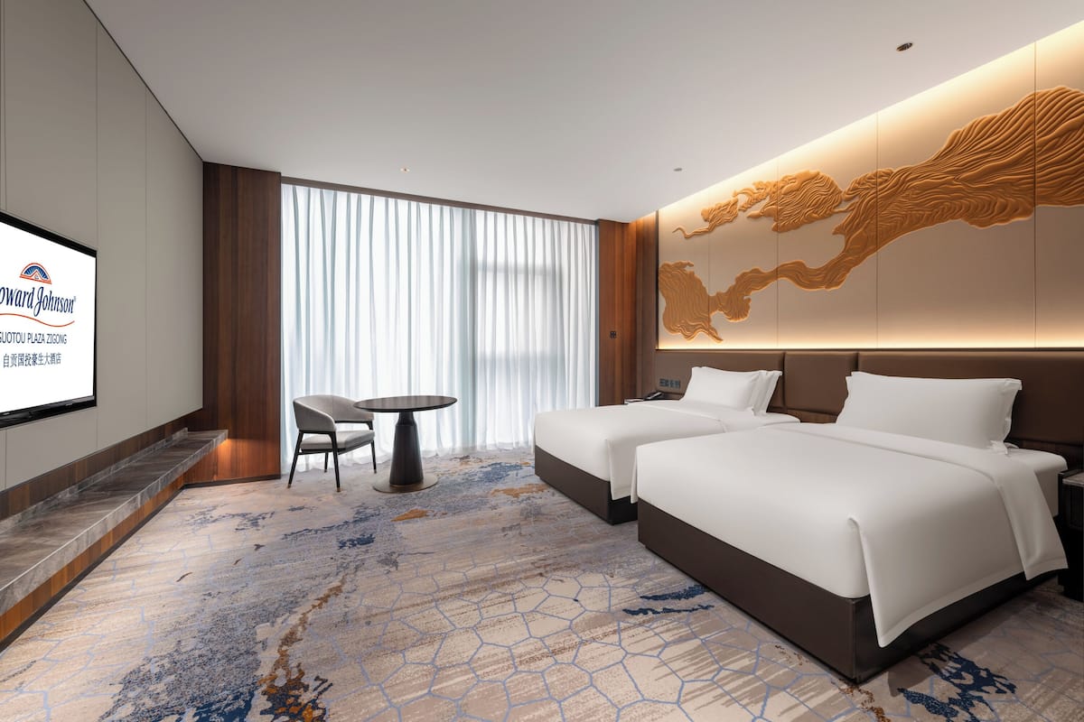 A hotel room with a large bed, a desk, and a TV on the wall.