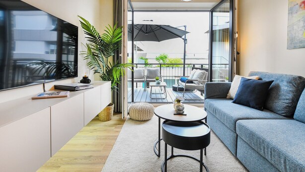 Una sala de estar moderna con un sofá, televisor, una mesa de centro y un balcón con mobiliario exterior.