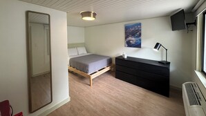 A bedroom with a bed, a dresser, a mirror, a painting, and a TV on the wall.