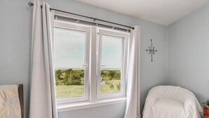 Un dormitorio con un ventanal grande, una cama, una silla y una brújula en la pared.