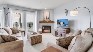 Una sala de estar con chimenea, televisor y balcón con cortinas.