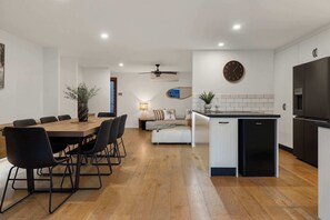 Una cocina moderna con refrigerador empotrado, una zona de comedor con mesa y sillas de madera, y un área de estar con sofá y una mesita auxiliar.